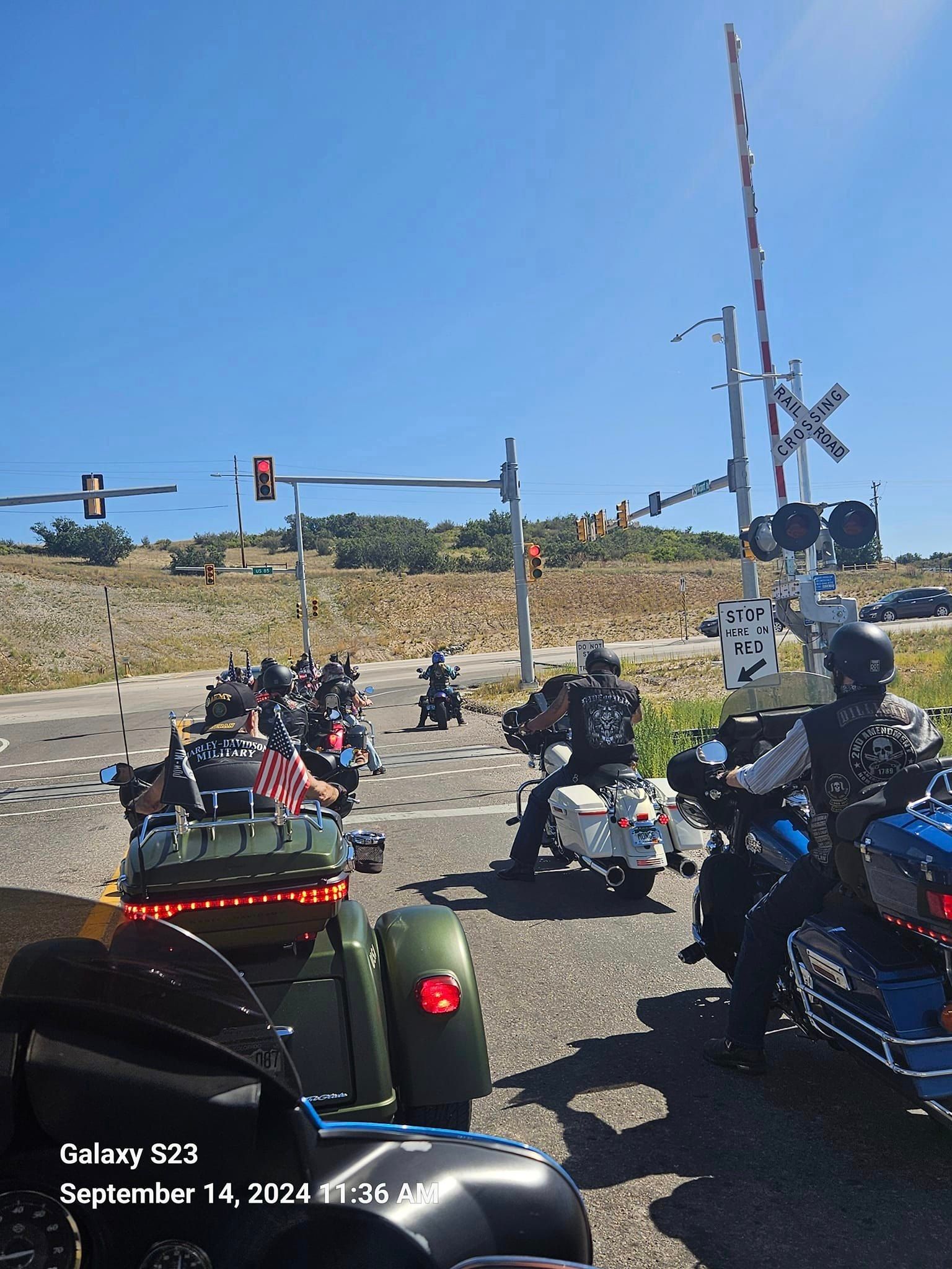 A group of motorcycles are driving down a road next to a railroad crossing.