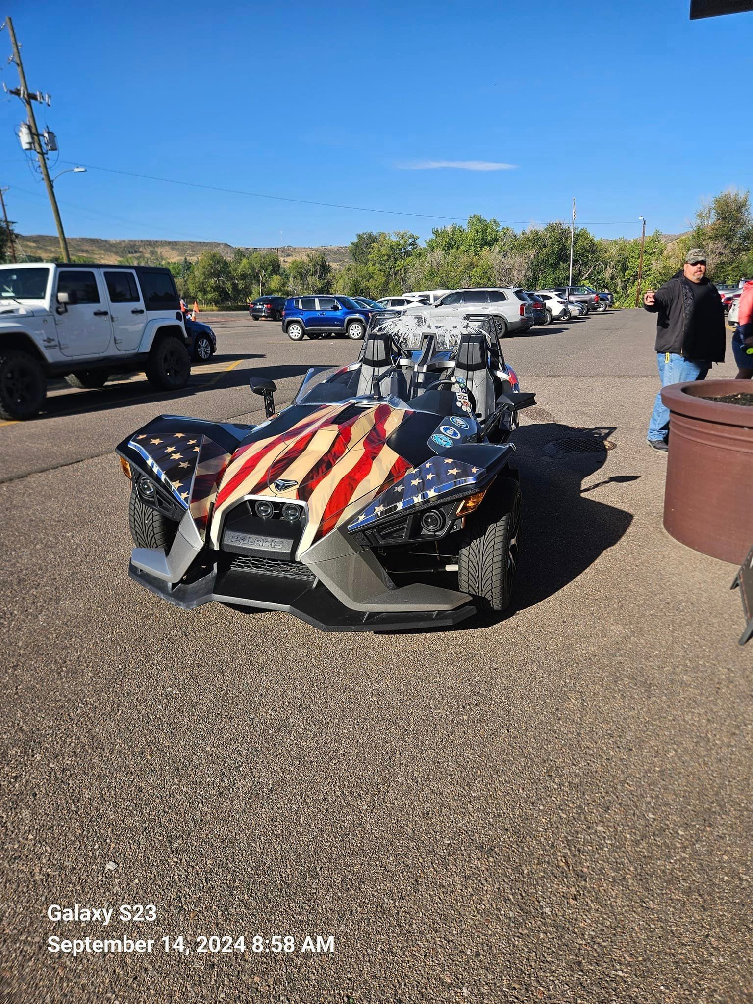 A slingshot with an american flag painted on it is parked in a parking lot.