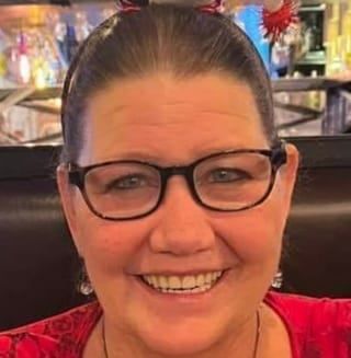 A woman wearing glasses and a red shirt is smiling for the camera.