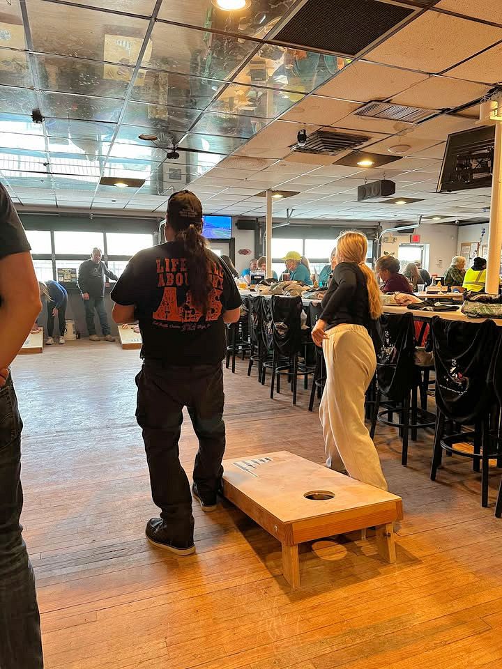 A man and a woman are playing cornhole in a restaurant.