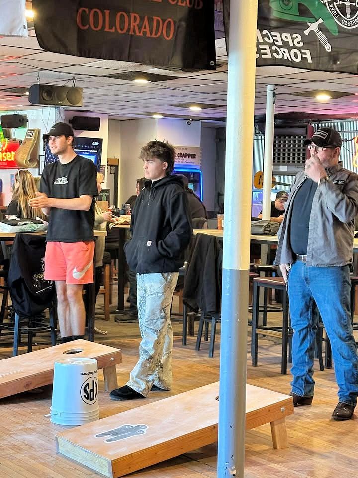 A group of people are standing in a room playing a game of cornhole.