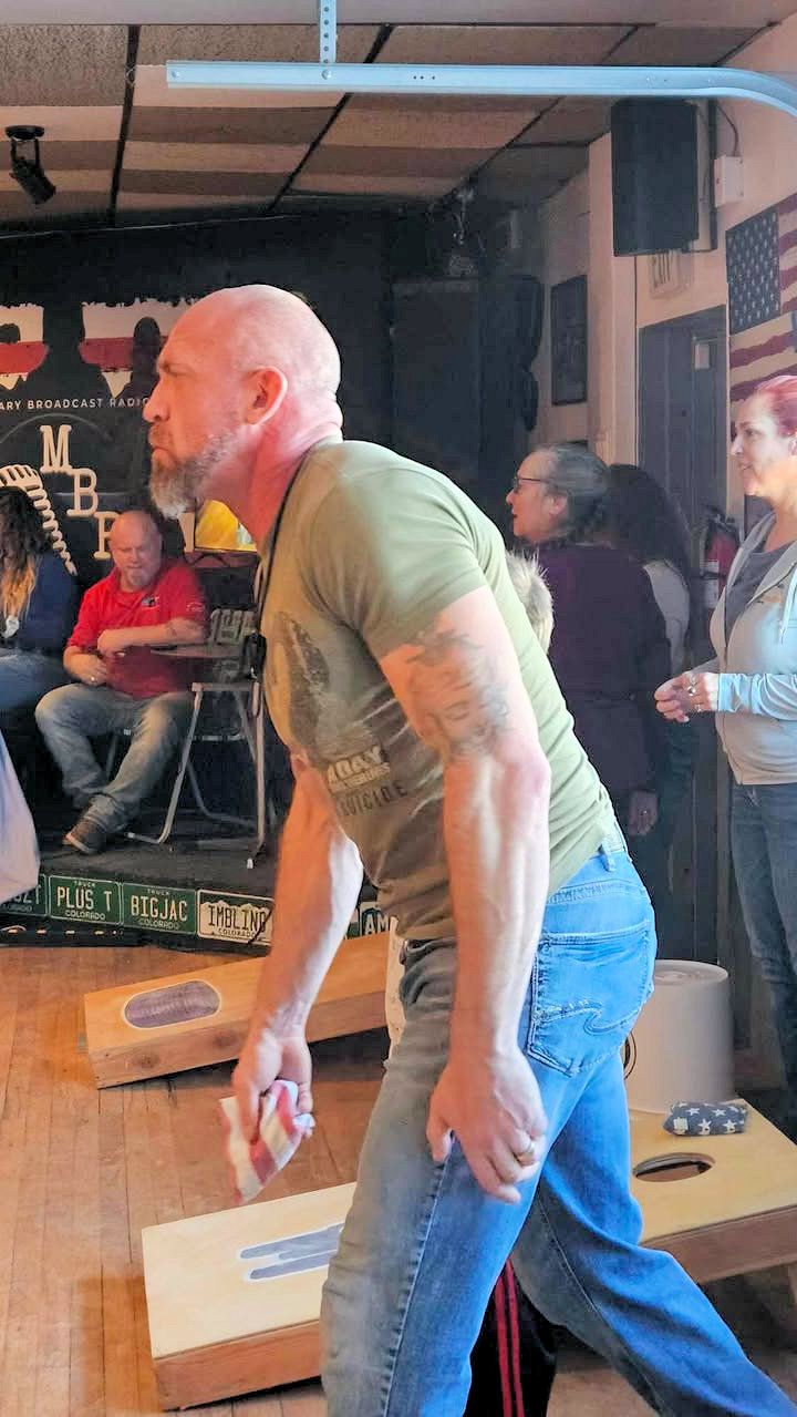 A man is playing a game of cornhole in a room.