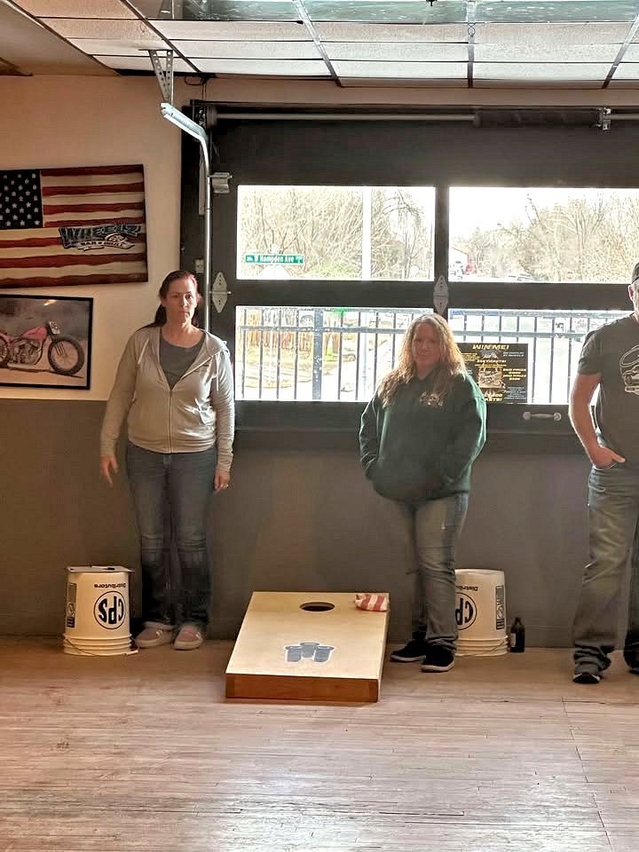A group of people standing next to a cornhole board in a room.