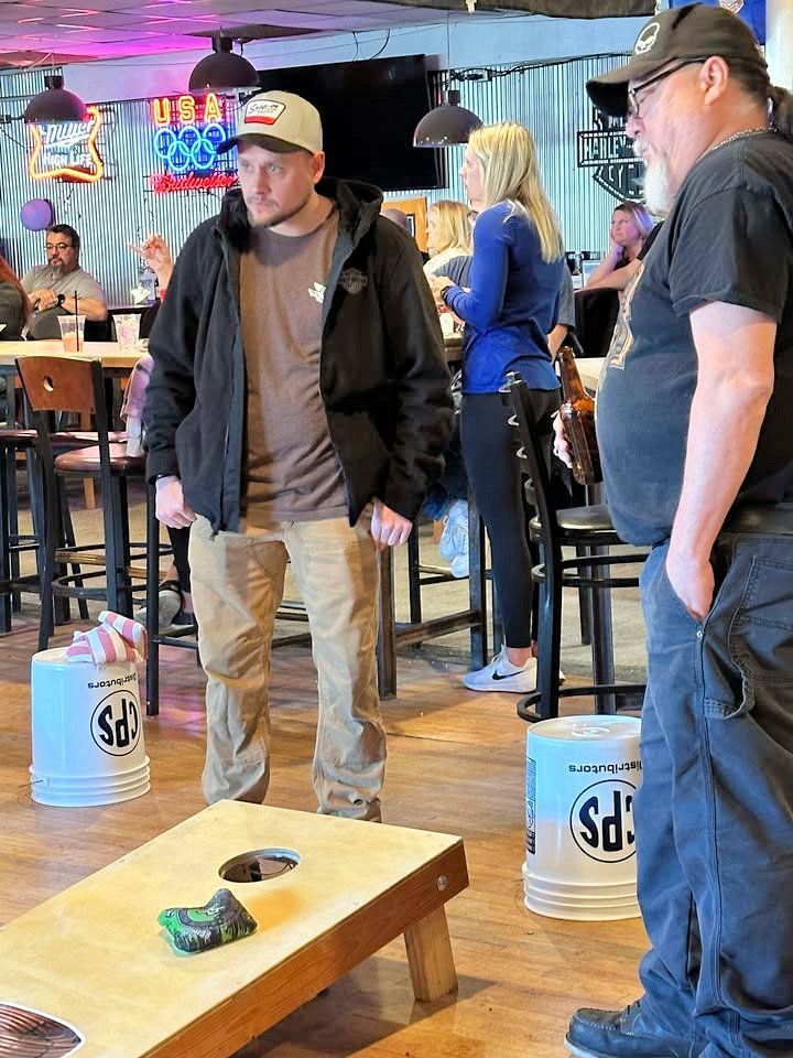Two men are standing next to a cornhole board in a restaurant.