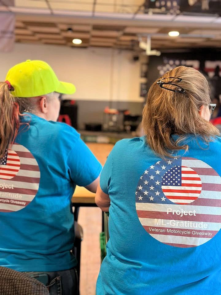 Two women wearing blue shirts with an american flag on the back are sitting at a table.