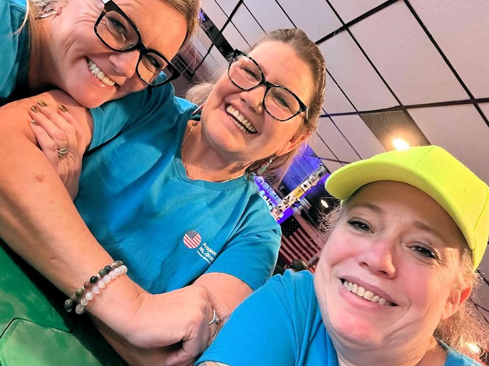 Three women wearing blue shirts and yellow hats are posing for a picture.