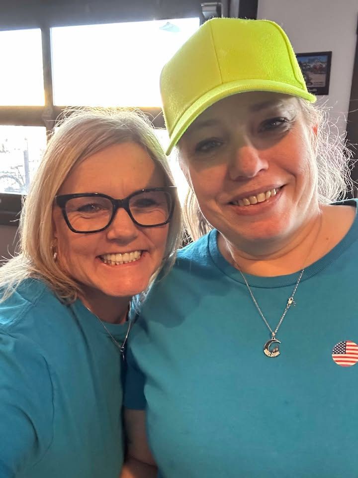 Two women wearing blue shirts and yellow hats are posing for a picture.