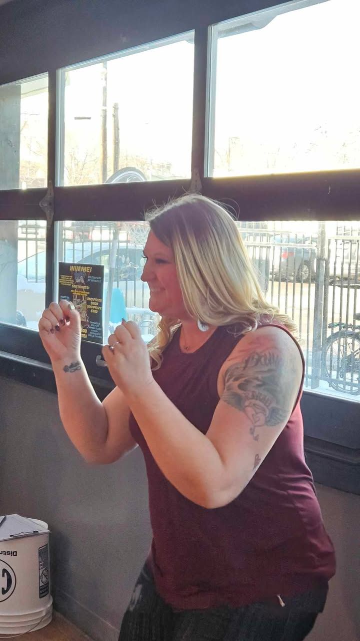 A woman with a tattoo on her arm is standing in front of a window.
