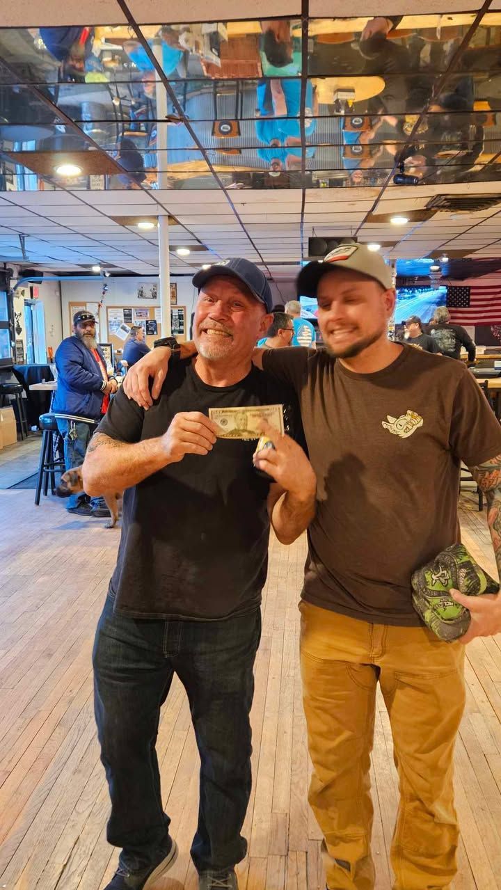Two men are standing next to each other in a room holding money.