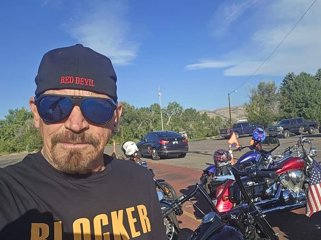 A man wearing sunglasses and a hat is standing in front of a row of motorcycles.