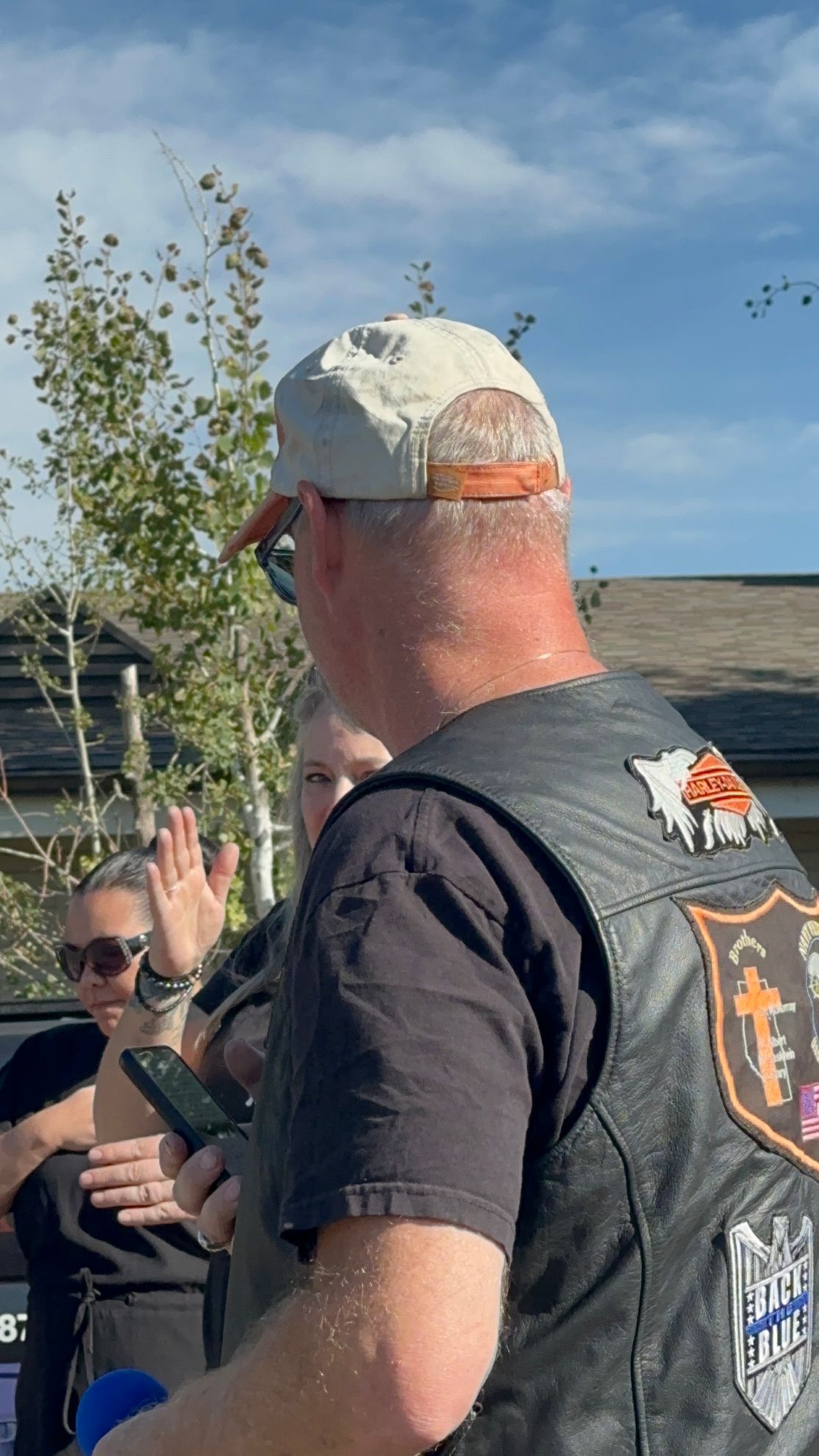 A man wearing a hat and a leather vest is standing in front of a group of people.