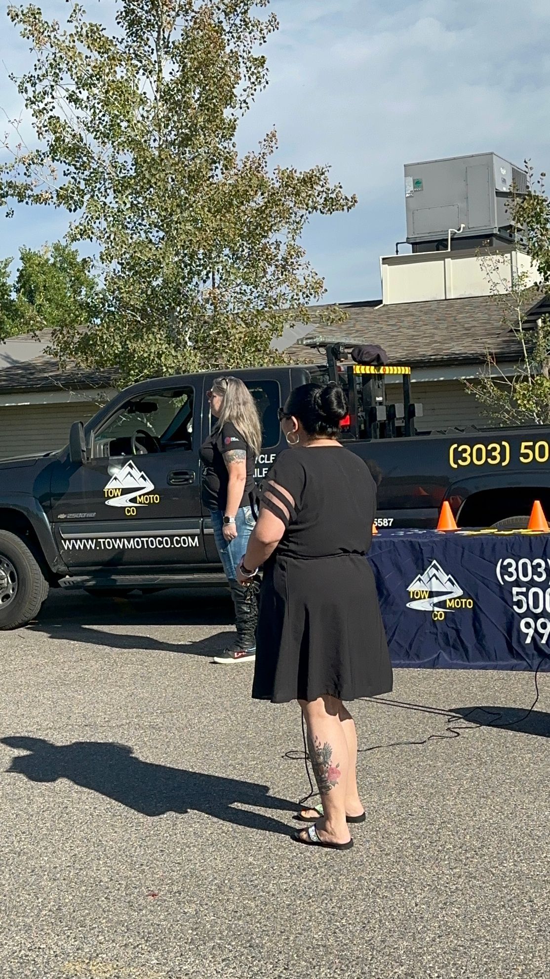 A woman in a black dress is standing in front of a tow truck.