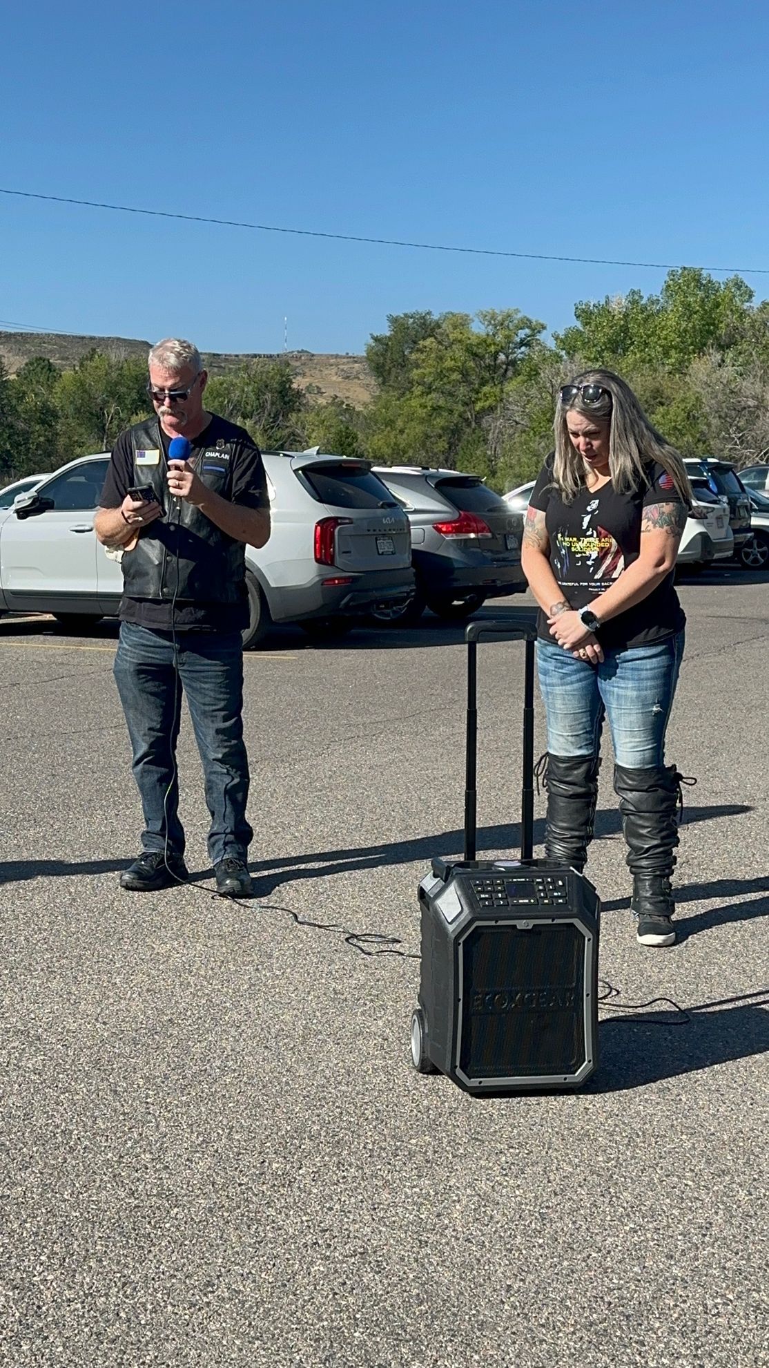 A man and a woman are standing next to a speaker in a parking lot.