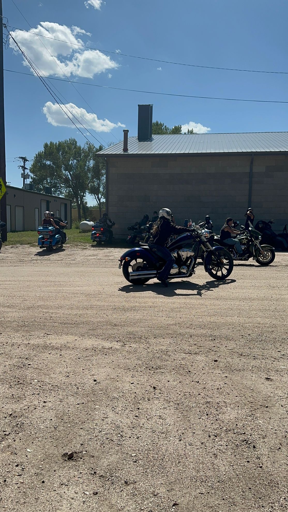A group of motorcycles are parked in a gravel lot in front of a building.
