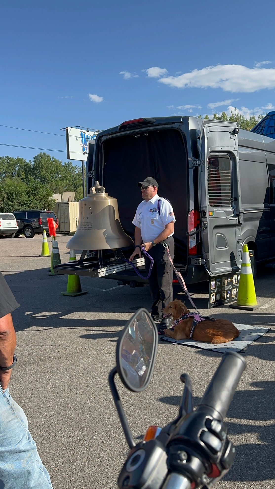 A man is standing in front of a van with a bell in it.