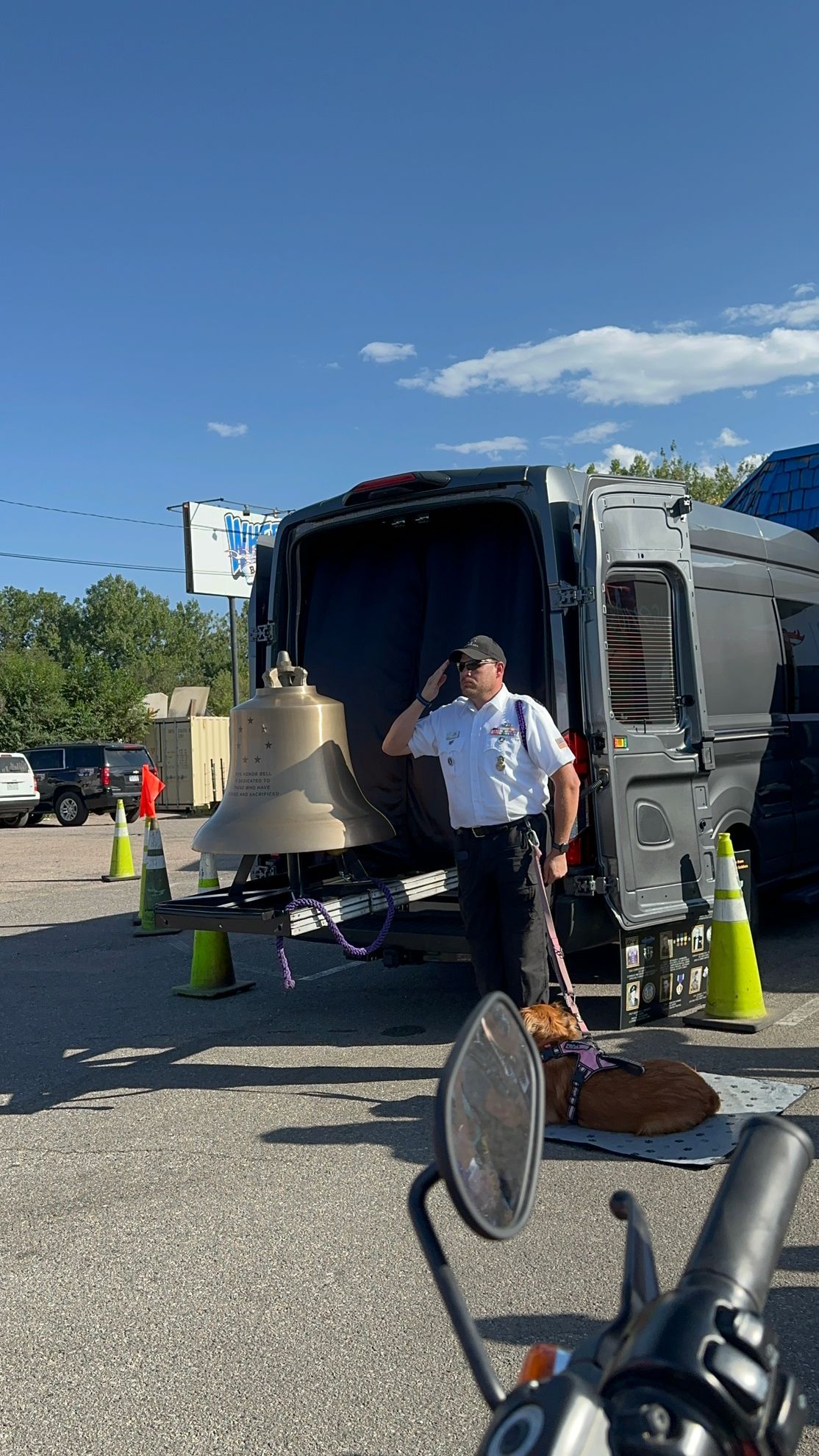 A man is standing in front of a van with a bell in it.