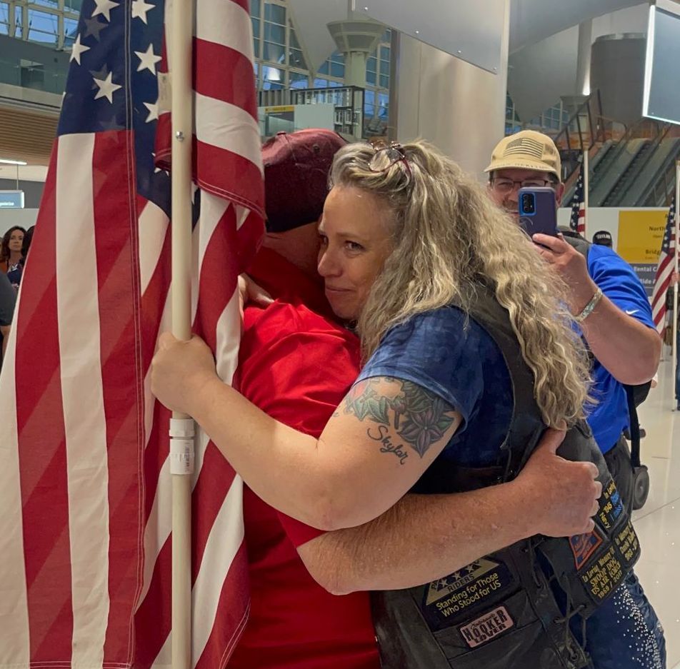 A woman hugging a man in front of an american flag