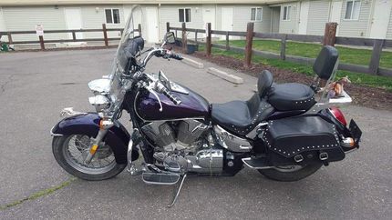 A purple motorcycle is parked in a parking lot in front of a house.