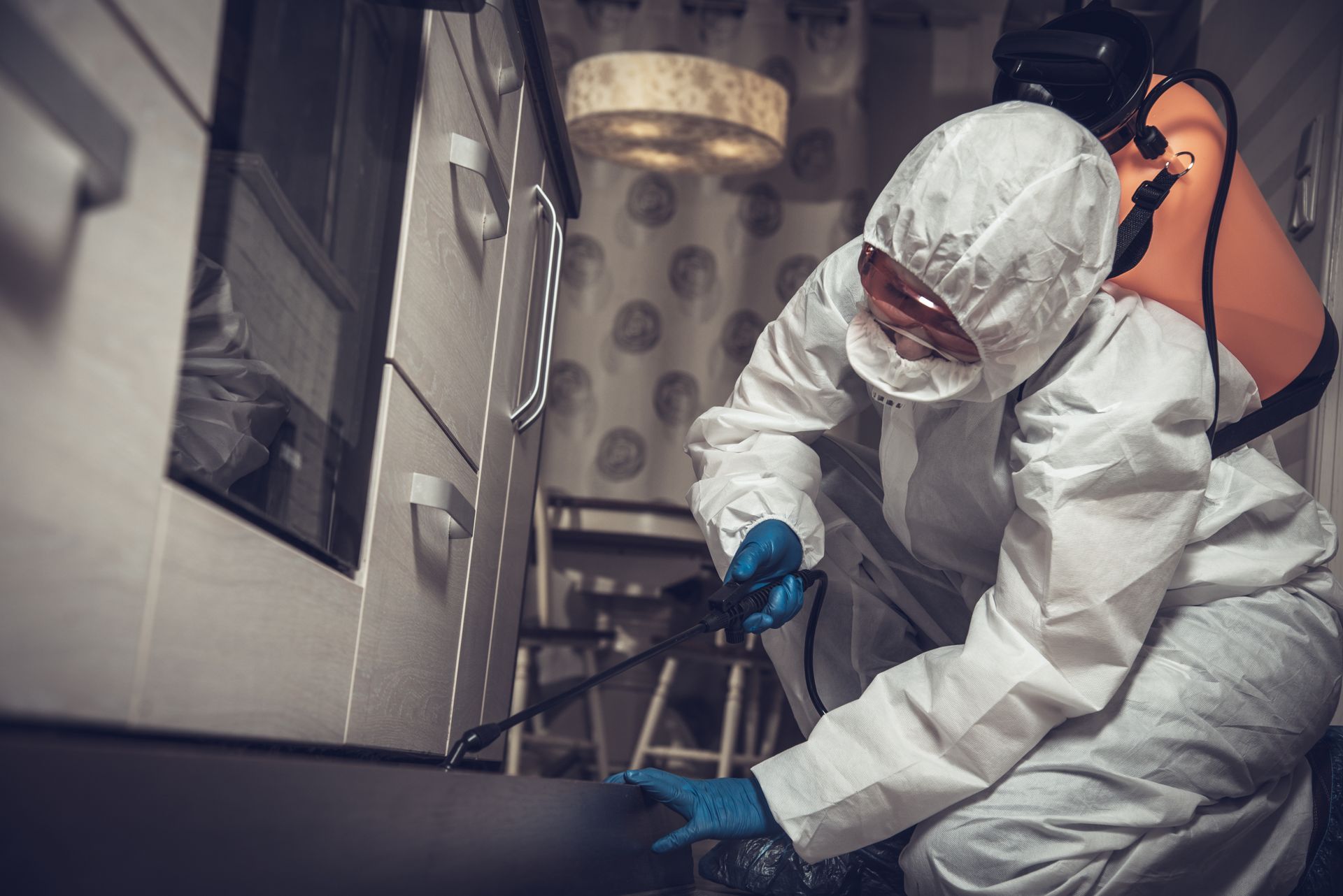 Technicians in white hazmat suits disinfecting a room with a spray wand