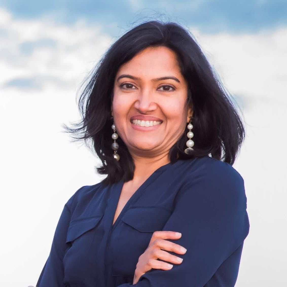 Smiling woman in a navy blouse with crossed arms against a cloudy sky background