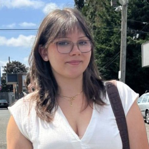 Woman wearing glasses and a white top standing outdoors on a sunny street