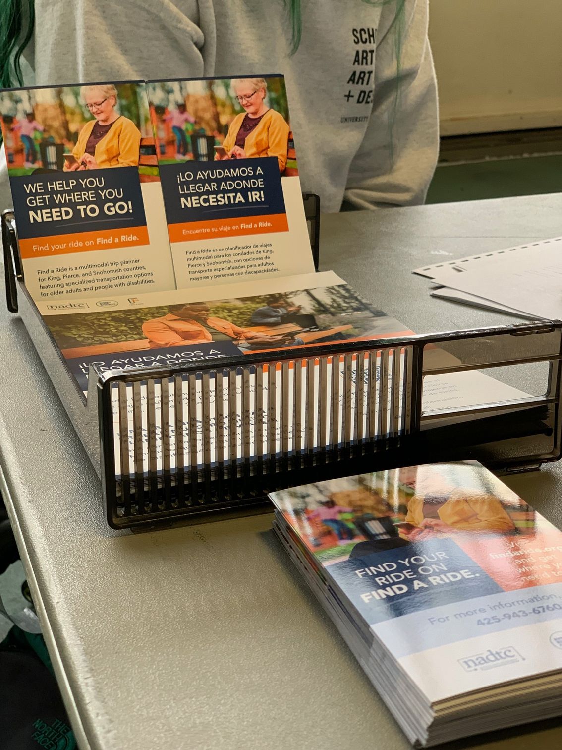 Branded materials for Find a Ride in Spanish and English with the blue and orange branding themes. Photo of woman on her phone with glasses and short grey hair. 