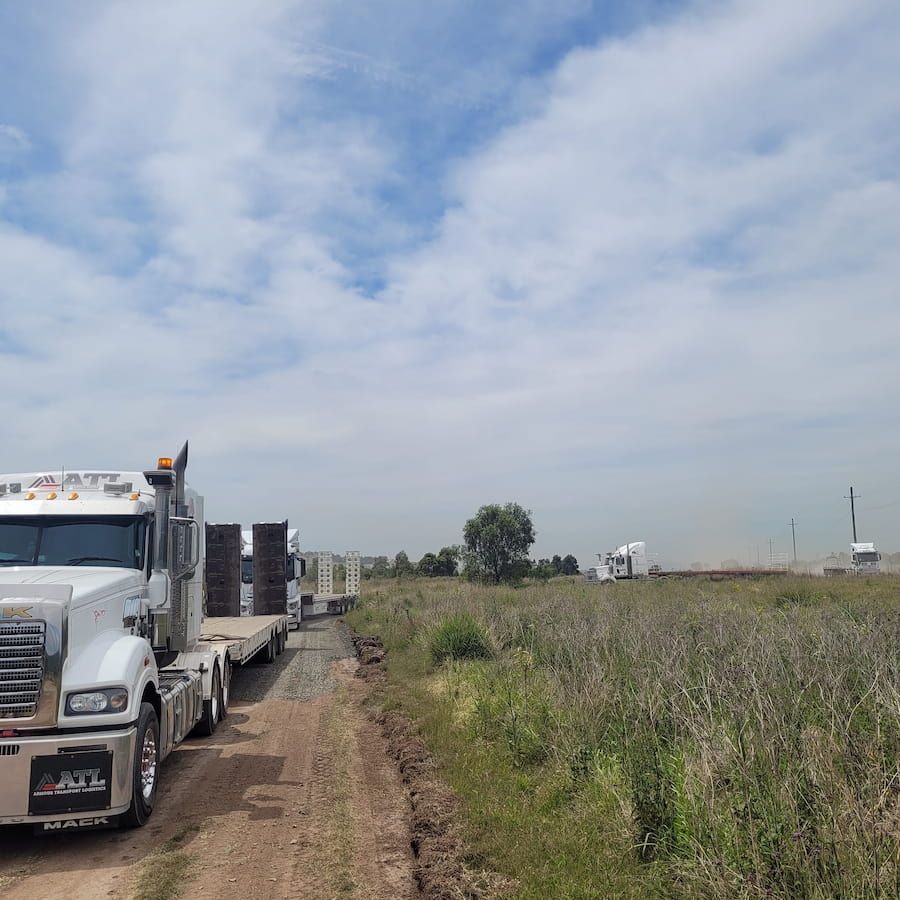 A Row Of Semi Trucks Are Parked On A Dirt Road — Armour Transport Logistics In Maitland, NSW