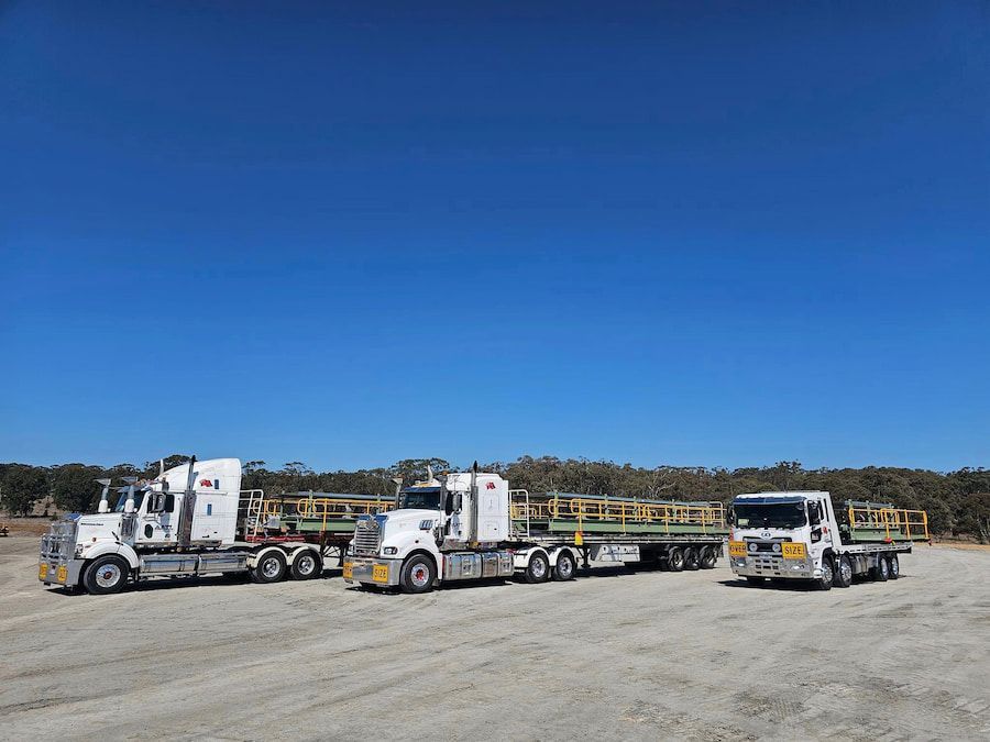 Three Semi Trucks Are Parked Next To Each Other On A Dirt Road — Armour Transport Logistics In Muswellbrook, NSW