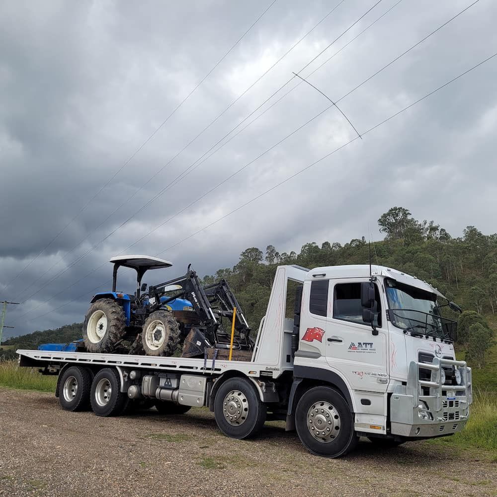 A White Truck With A Tractor On The Back Of It — Armour Transport Logistics In Singleton, NSW