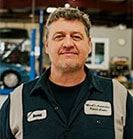 Mechanic in a blue uniform smiles in a garage. | Emge's Car Craft Auto Services