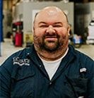 Man in navy work shirt, smiling, in a garage setting. | Emge's Car Craft Auto Services