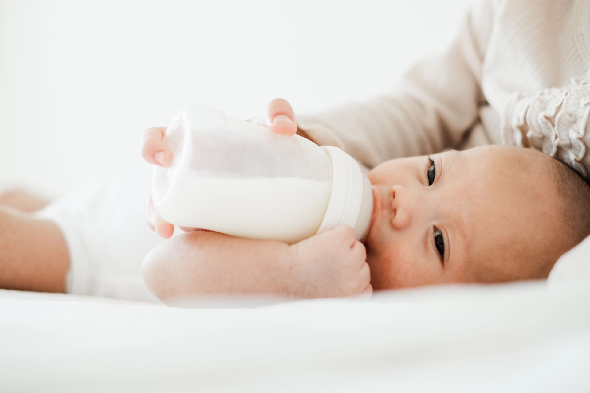Bambino sdraiato su un lettino bianco, che beve dal biberon