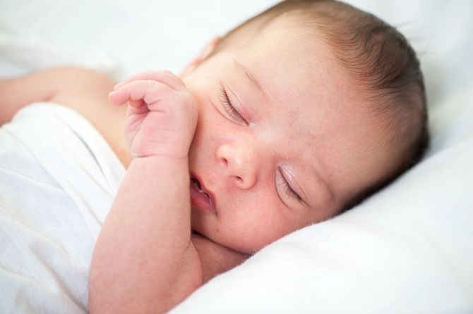 Neonato addormentato avvolto in una coperta bianca, appoggiato su un morbido cuscino.