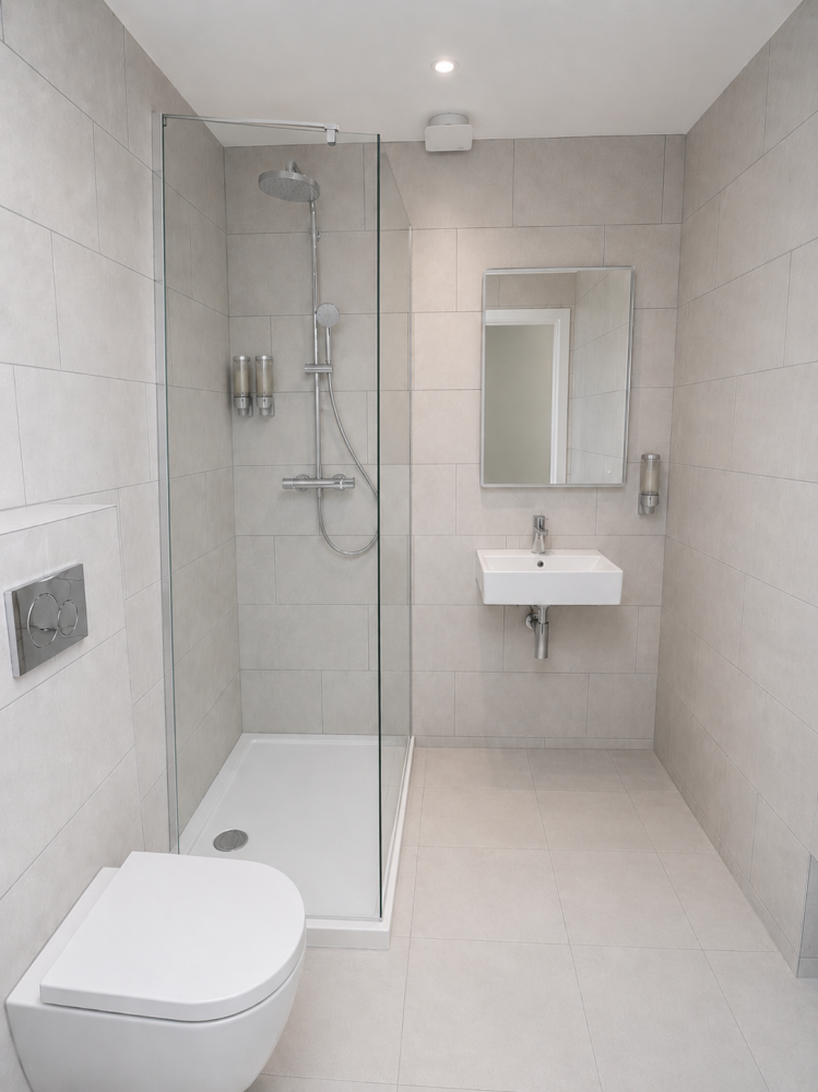 Modern tiled bathroom with a glass shower, wall-hung toilet, sink, and mirror.