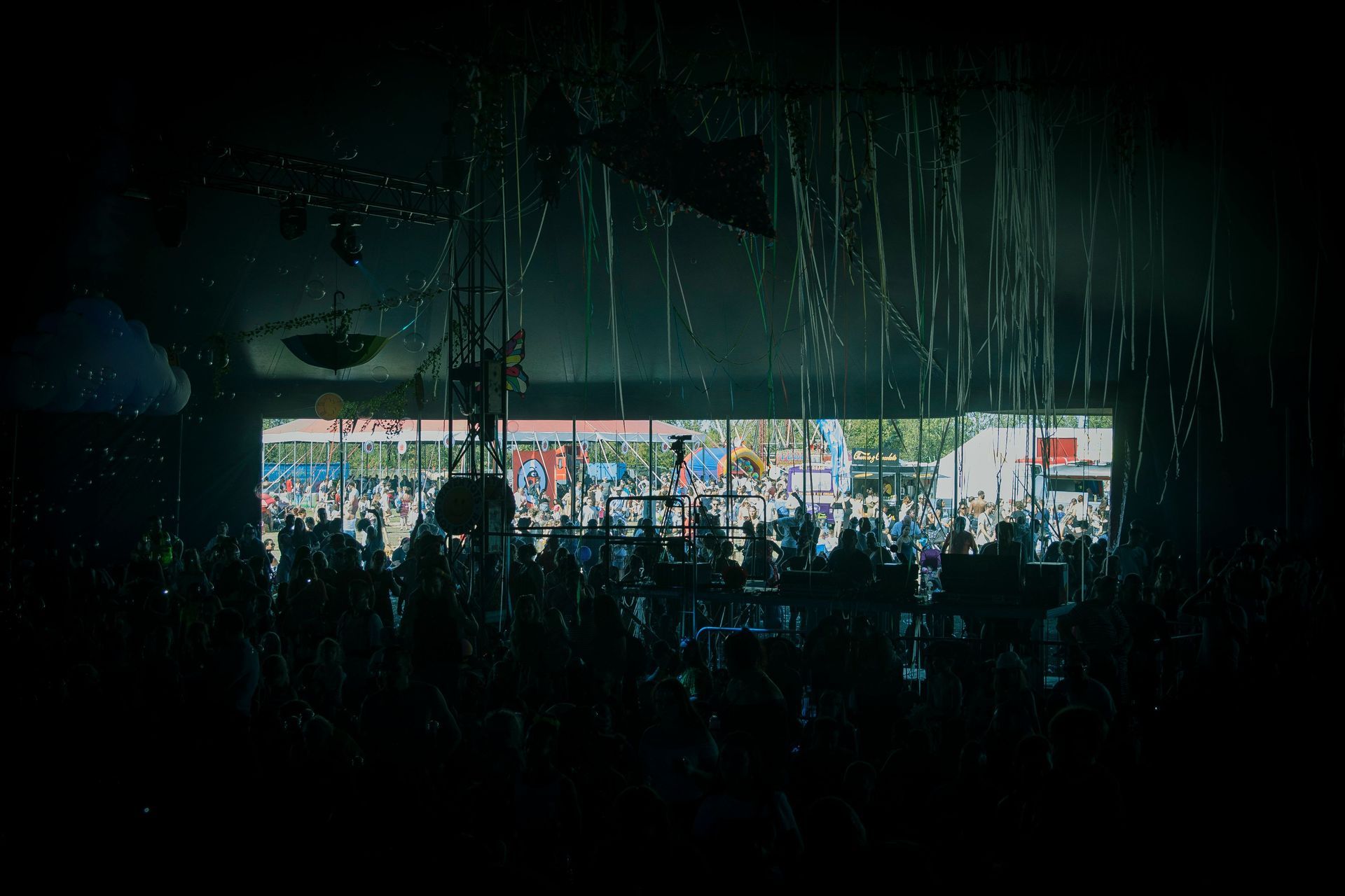 Crowded dim indoor scene with a bright storefront or stage and hanging strands in the foreground
