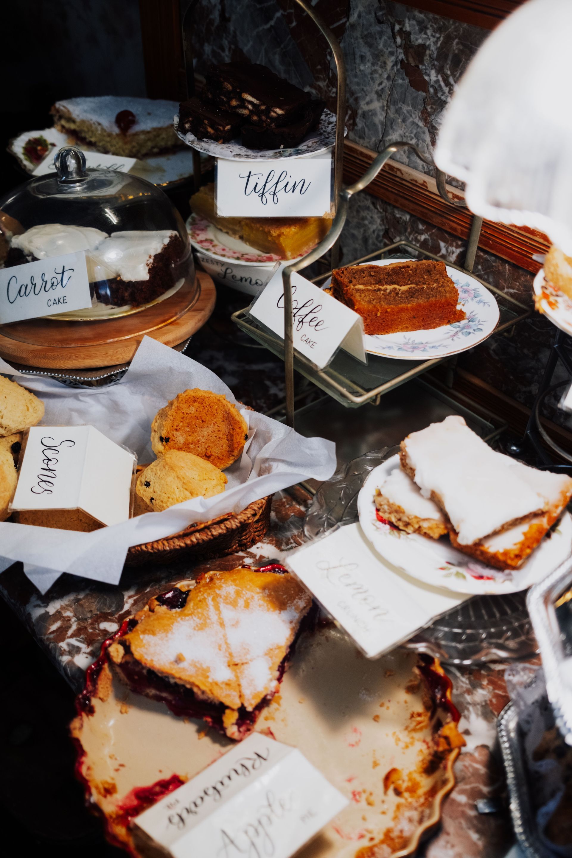Assorted pastries on plates in a bakery display case, with labels and chocolate-drizzled slices.