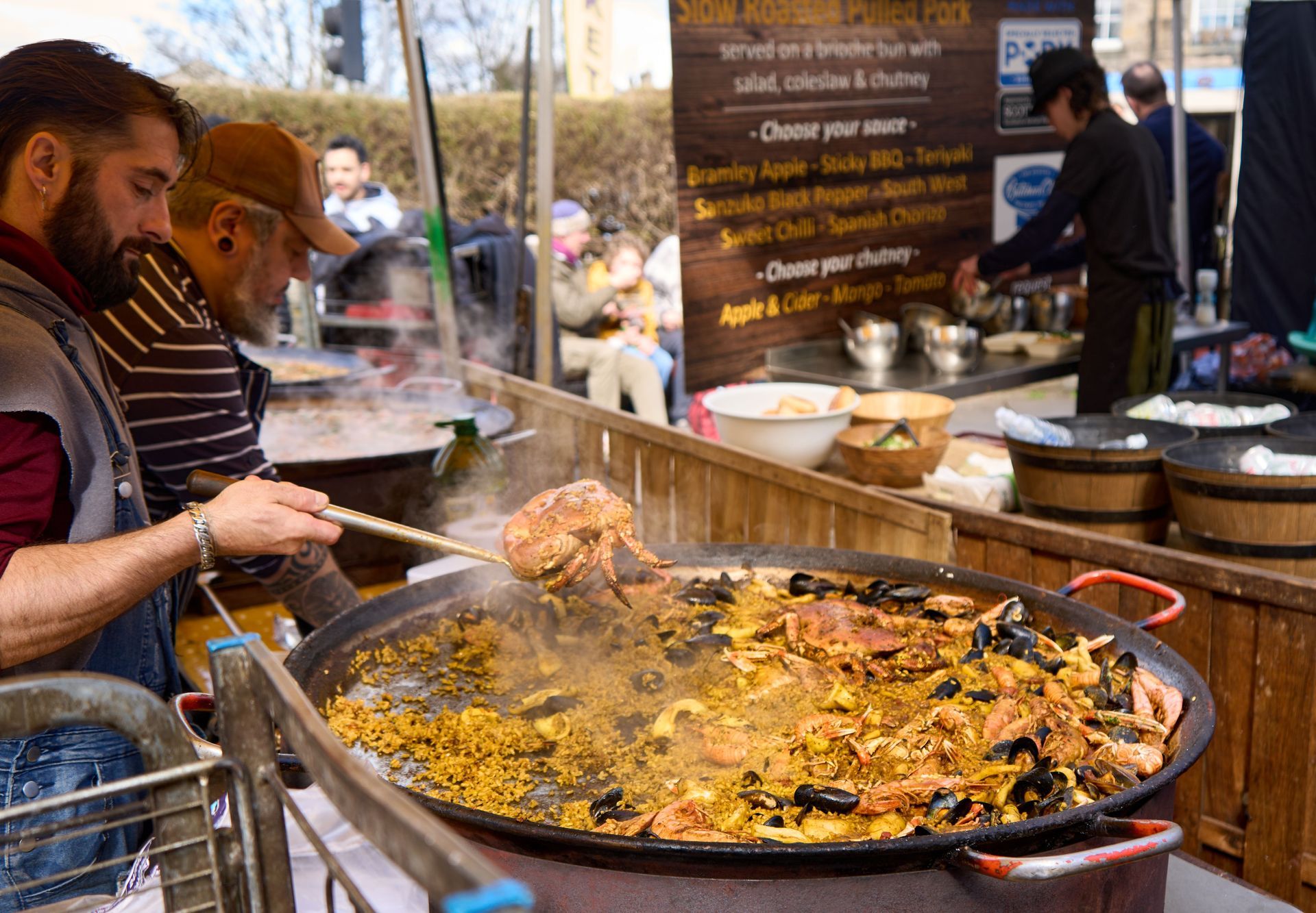Street food stall with two people stirring a large steaming pan of paella outdoors