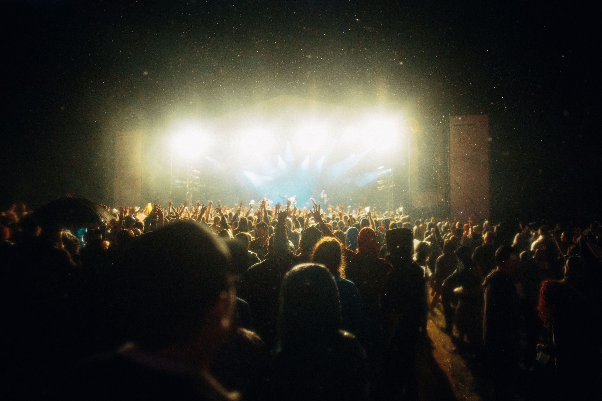 Crowd at a nighttime concert, facing a brightly lit stage with intense white lights