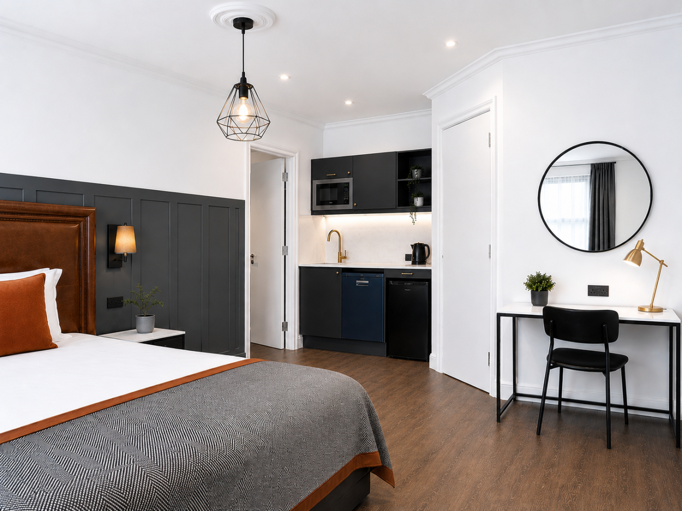 Modern bedroom with dark accent wall, bed, desk, mirror, and kitchenette area