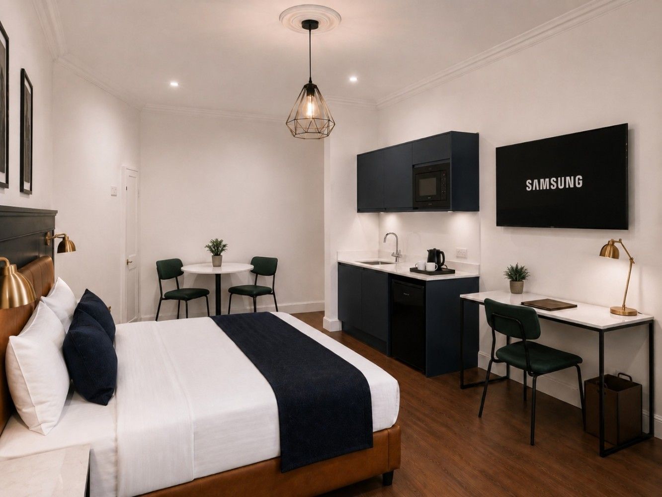 Modern studio apartment with a bed, desk, kitchenette, and wall-mounted Samsung TV
