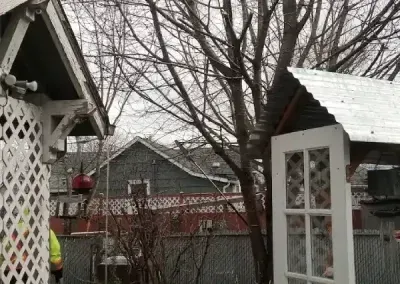 Snowy backyard with bare trees, small sheds, and a white gazebo under an overcast sky