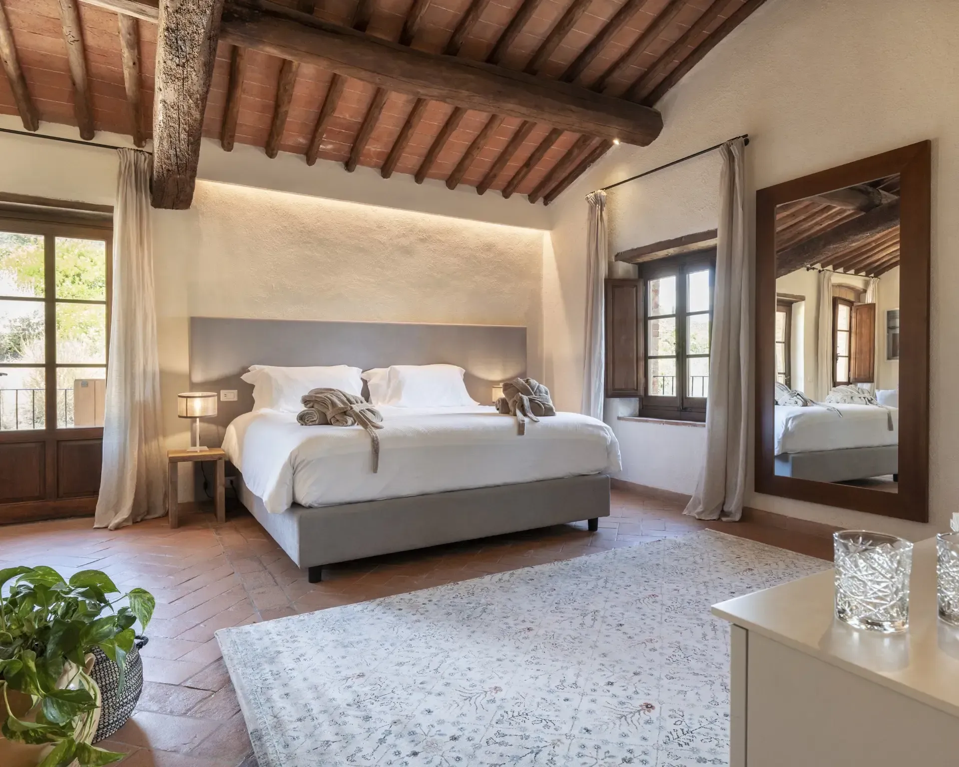 Bedroom with exposed wood ceiling, double bed, large mirror, and open doorway to outside.