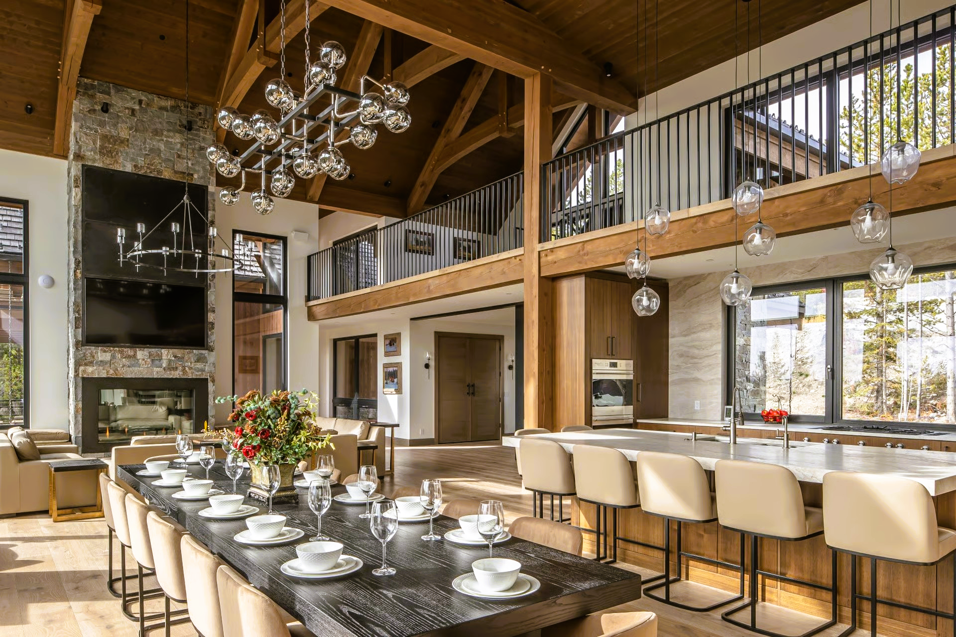 Spacious, light-filled dining area with long table and island seating, high ceilings, and a stone fireplace.