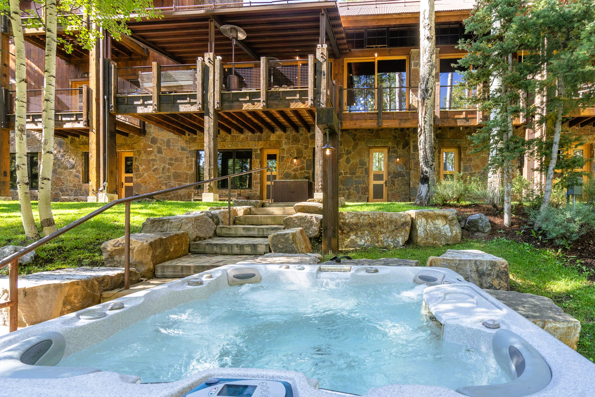 Hot tub in a stone yard with a multi-level wood and stone house.