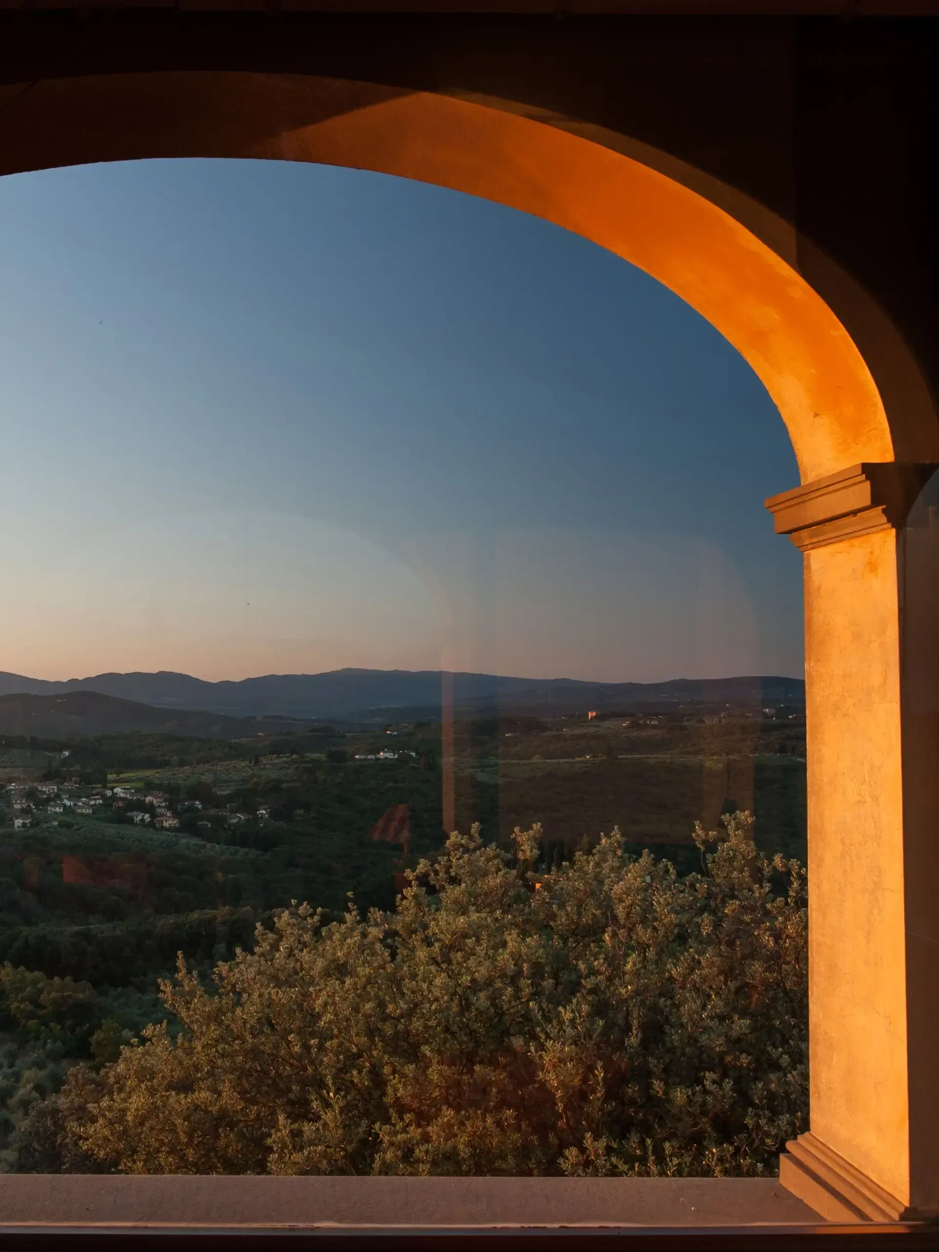 An archway frames a sunset view of a valley. Orange light illuminates the arch and highlights the landscape.