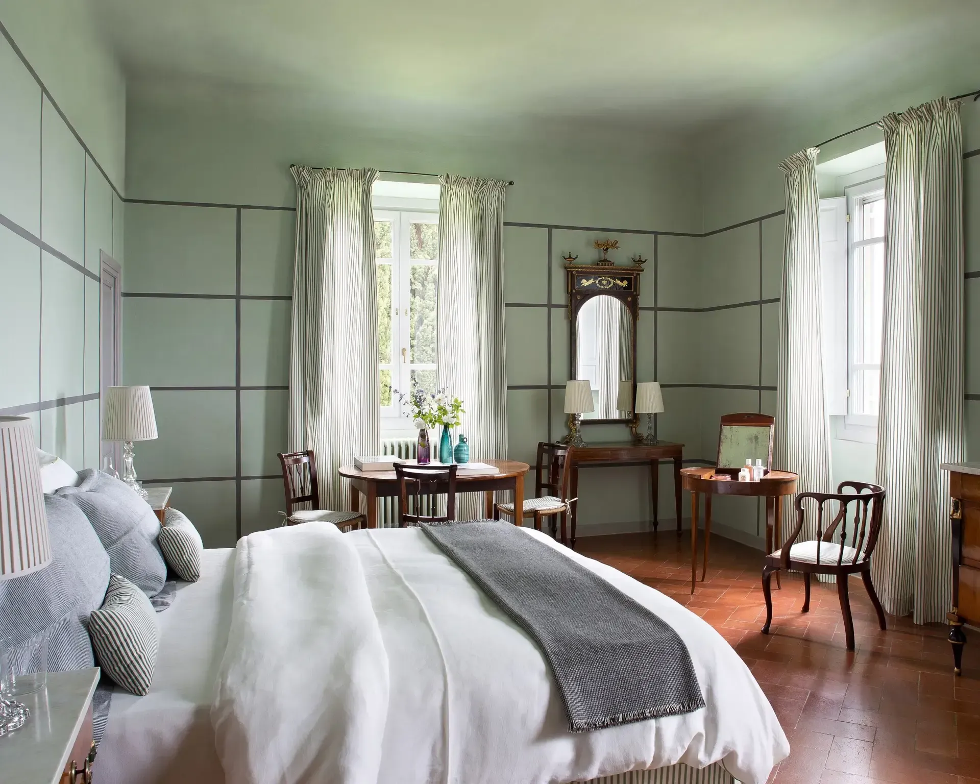 Elegant bedroom with pale green walls, bed, wooden furniture, and patterned curtains.