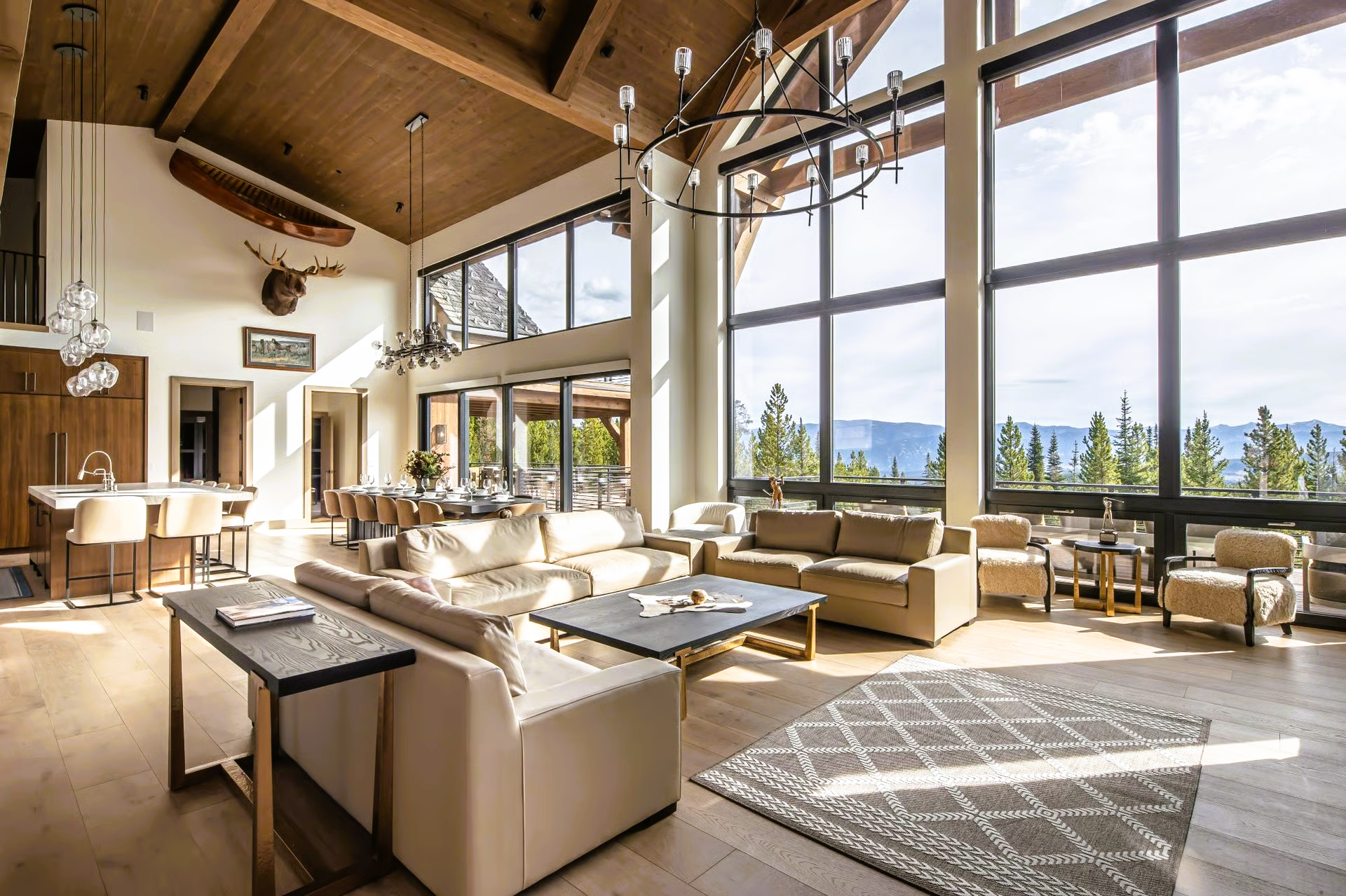 Spacious living room with large windows overlooking a mountain view. Furnished with neutral-toned sofas, rug, and chairs.