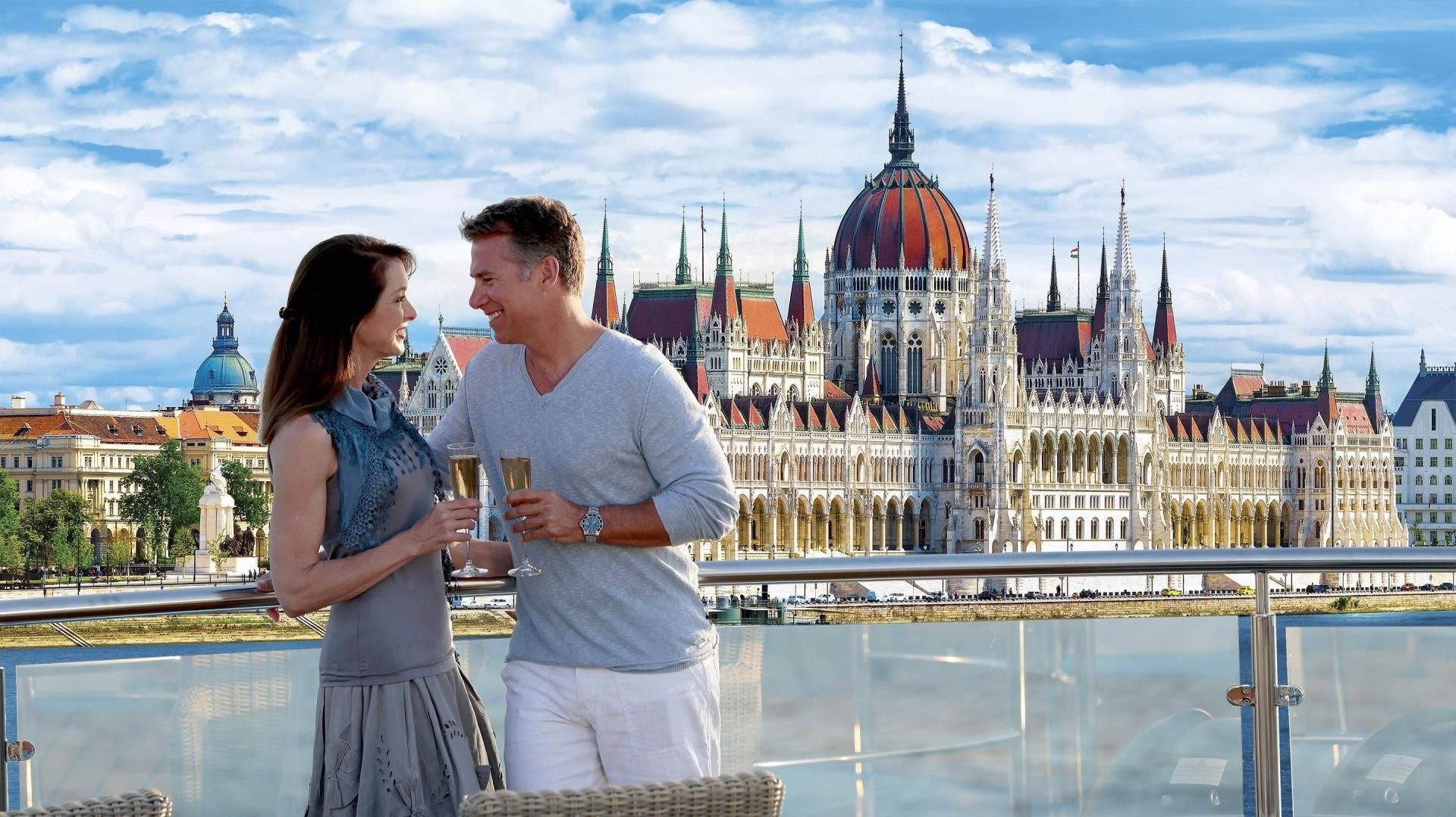 Couple toasting champagne on a deck overlooking the Hungarian Parliament Building in Budapest.
