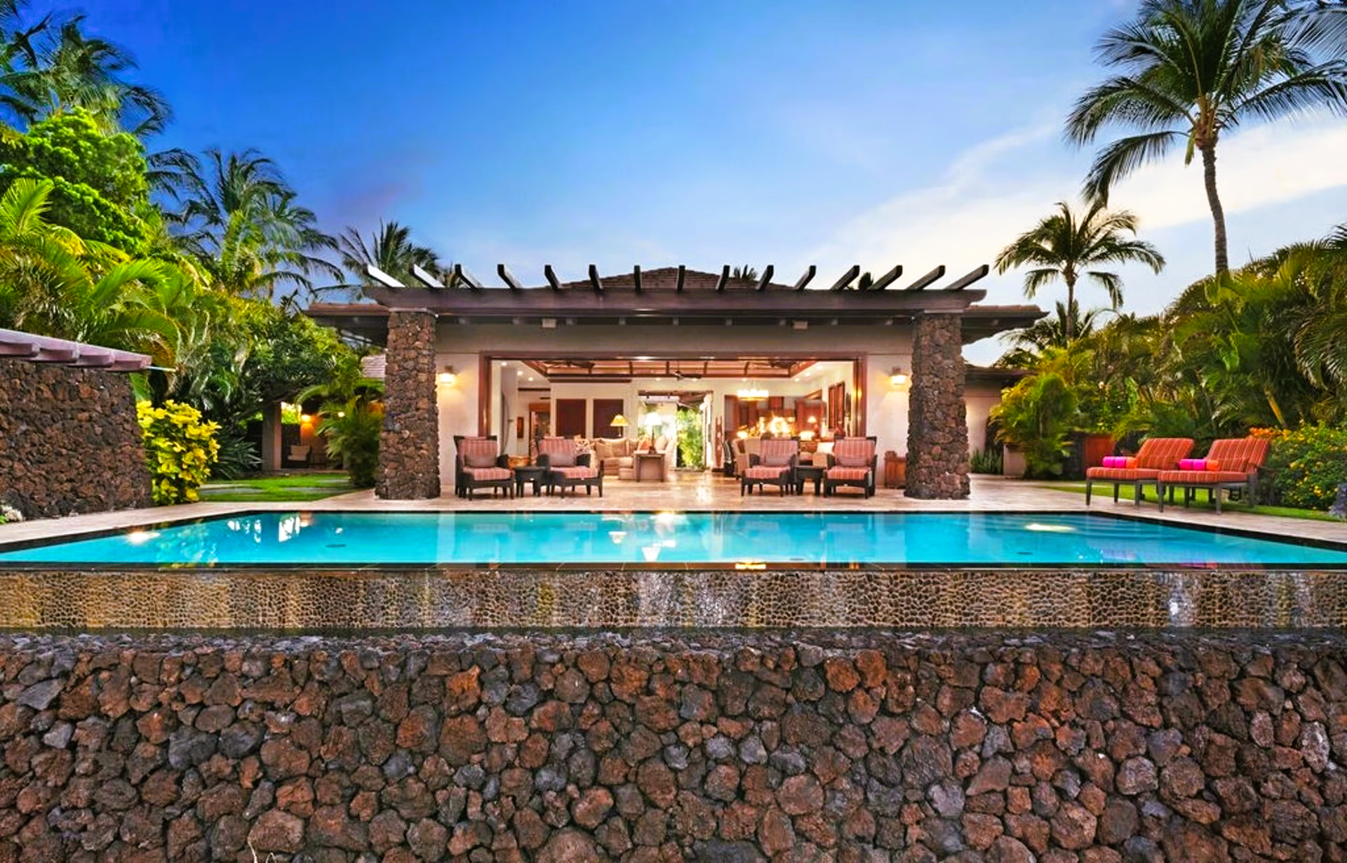 Poolside luxury home with infinity pool; tropical setting, sunset.