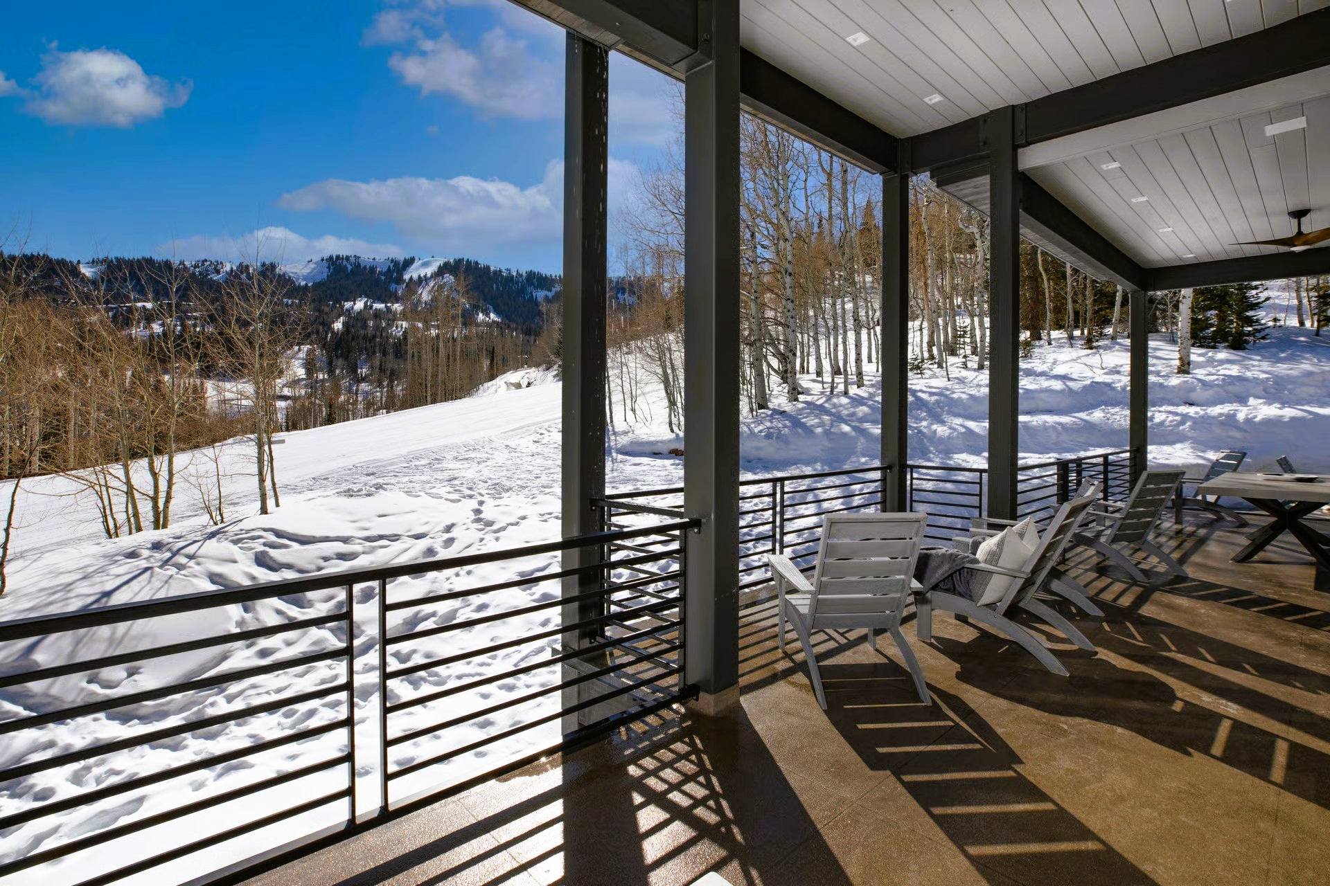 Covered patio overlooking snowy mountain landscape with trees and chairs.